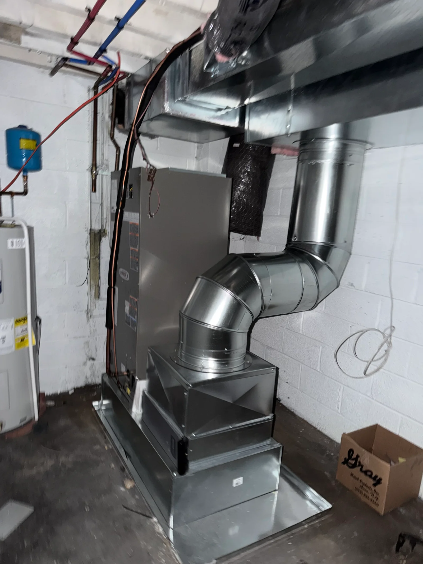 Galvanized steel ductwork connected to a furnace cabinet in a basement with white block walls and copper lines