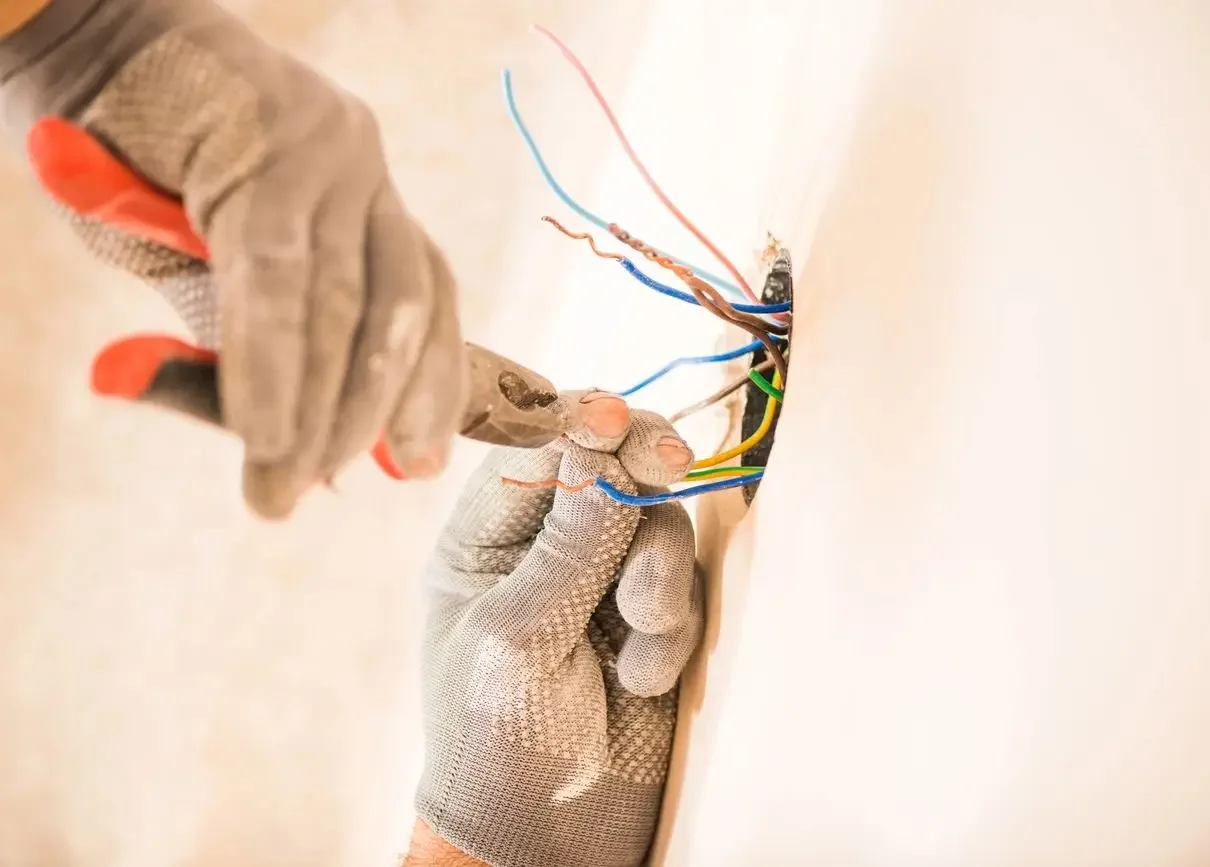 Gloved technician terminating blue, brown, red, and green-yellow wires at a recessed wall box with cutting pliers