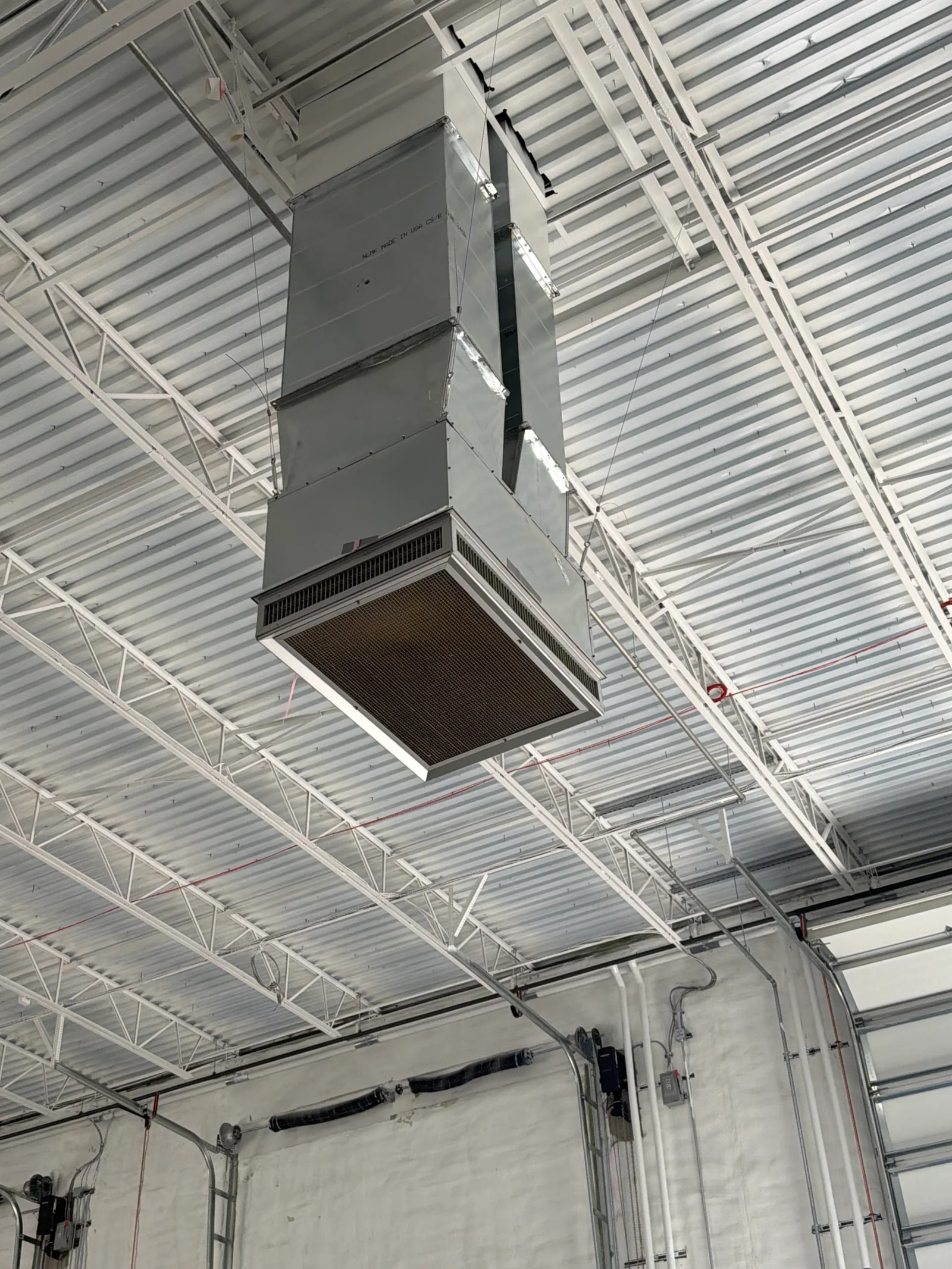 Suspended galvanized steel air handler with filter access panel hung from white painted steel trusses and corrugated metal roof deck