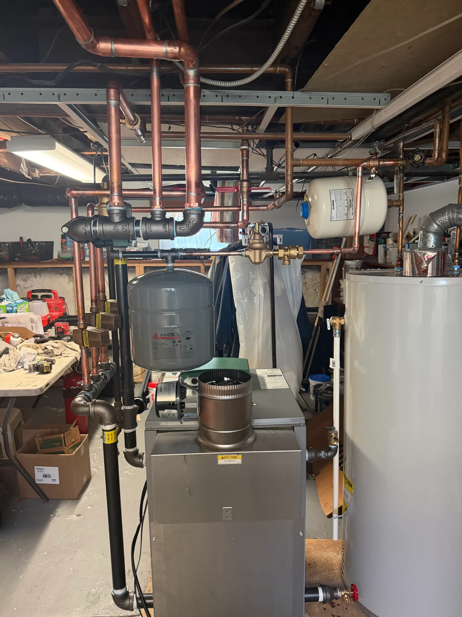Basement boiler room with stainless steel boiler, Amtrol expansion tank, copper and black iron piping, and circulator pumps