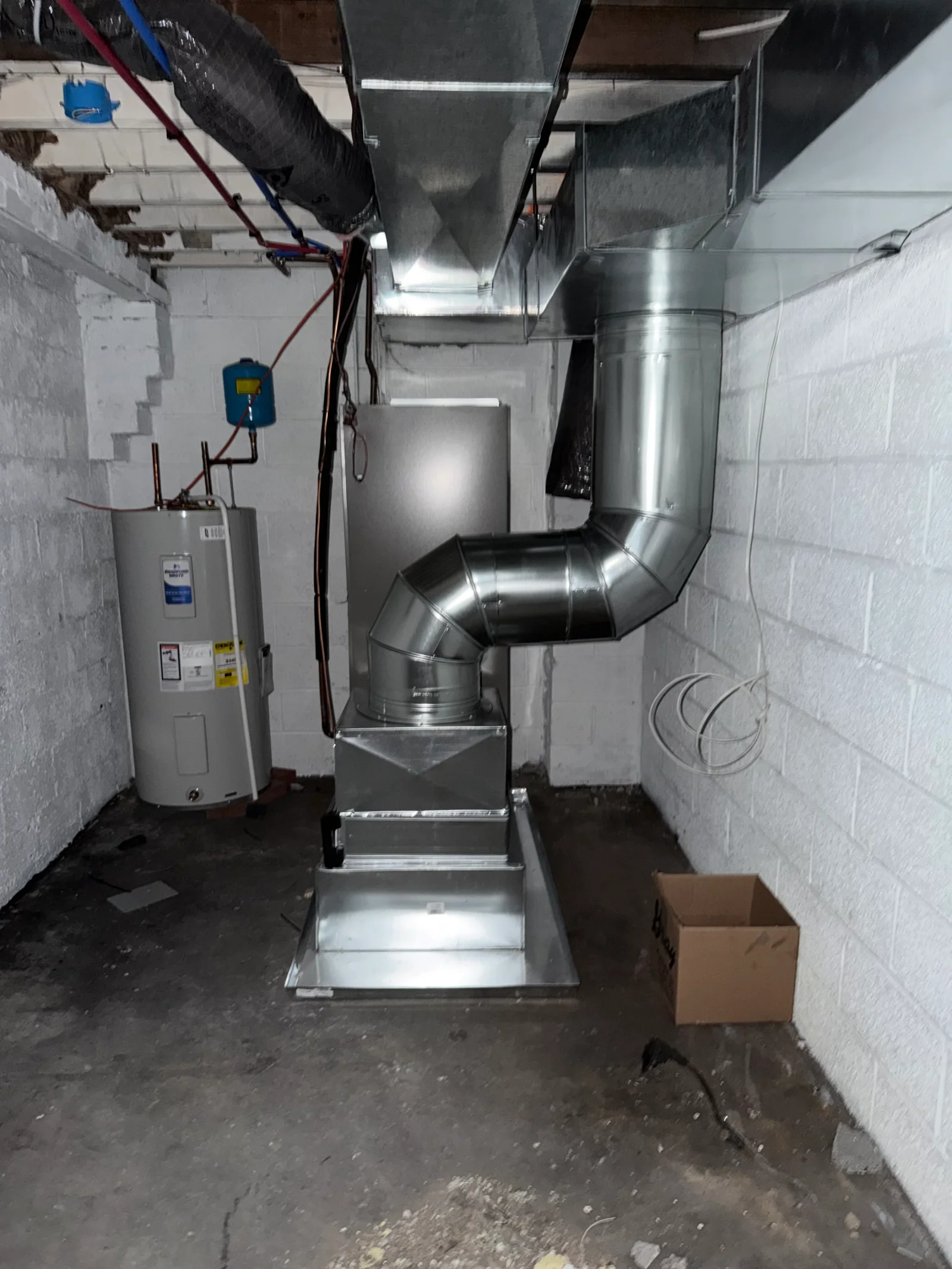 Galvanized furnace installation with round and rectangular metal ductwork in unfinished basement beside a water heater
